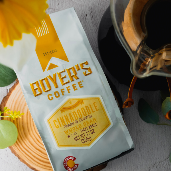 bag of cinnadoodle coffee next to a chemex on a wooden surface with yellow flowers.