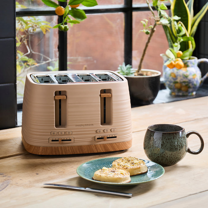 Beige toaster on a wooden table with a plate of food, knife, and mug in a kitchen setting.