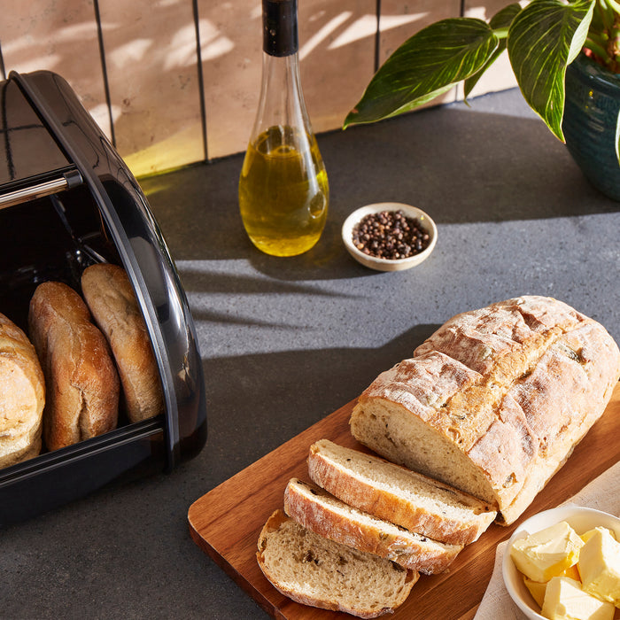 Loaf of bread sliced on a wooden board with a toaster and ingredients in the background.