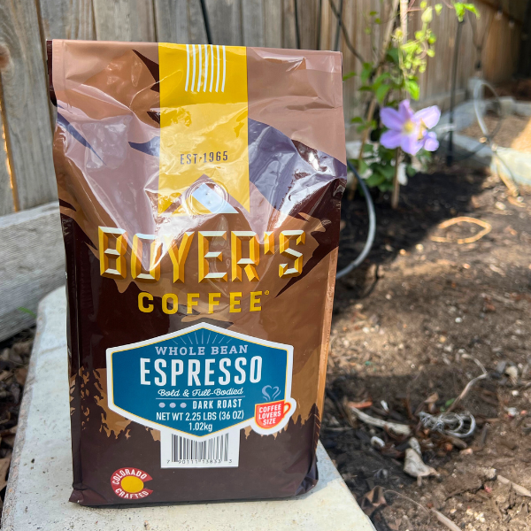Bayer's Coffee Whole Bean Espresso package on a stone surface with a garden background