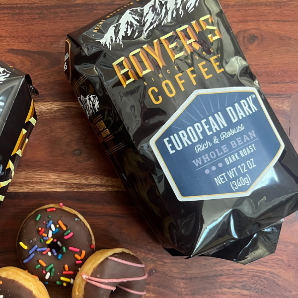 Boyer's Coffee European Dark roast coffee bag on a wooden surface with donuts.