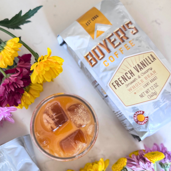 Boyer's Coffee French Vanilla package with a glass of iced coffee and flowers on a light surface
