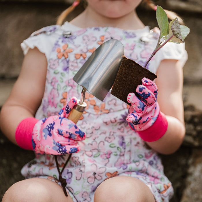 girl with pink gloves on holding flower and trowel